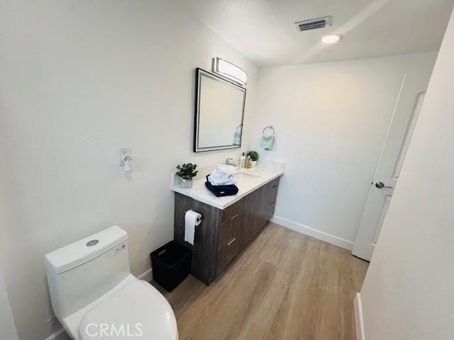 bathroom with vanity, toilet, visible vents, baseboards, and wood finished floors