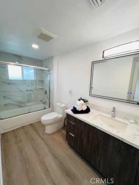 bathroom featuring vanity, toilet, combined bath / shower with glass door, visible vents, and wood finished floors