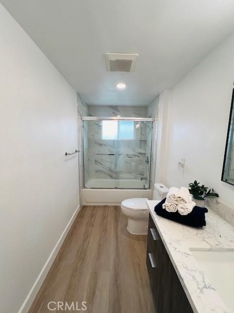 full bath featuring wood finished floors, combined bath / shower with glass door, toilet, vanity, and visible vents
