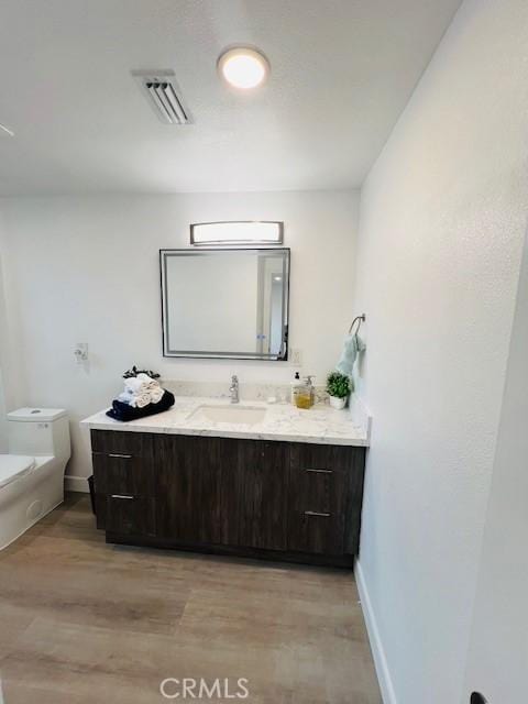 bathroom featuring wood finished floors, toilet, visible vents, and vanity