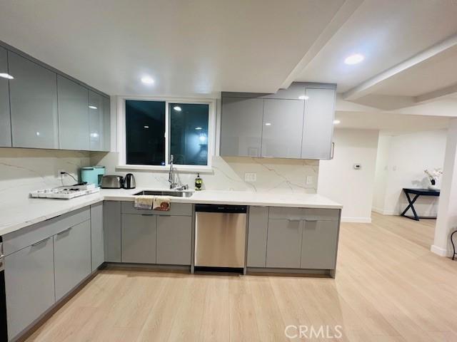 kitchen with a sink, modern cabinets, light wood-style floors, gray cabinets, and stainless steel dishwasher
