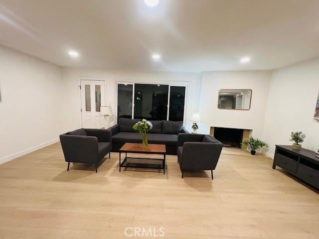 living area featuring light wood-type flooring, recessed lighting, and a fireplace with raised hearth