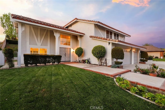 mediterranean / spanish house featuring concrete driveway, stucco siding, a tile roof, and a lawn