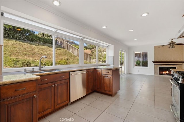 kitchen featuring stainless steel appliances, a sink, a tiled fireplace, light tile patterned flooring, and crown molding