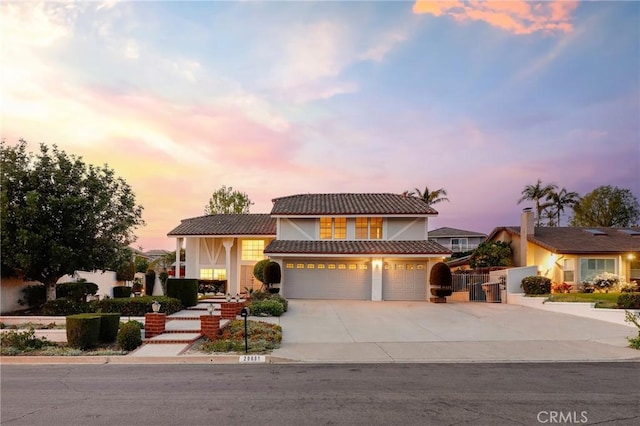 view of front facade with concrete driveway, an attached garage, stucco siding, a gate, and a tiled roof
