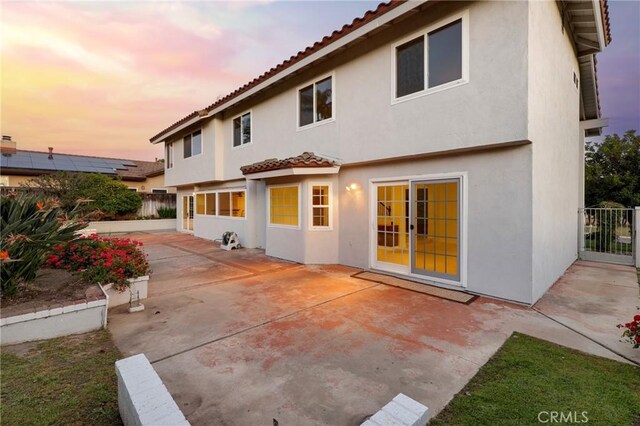 back of house at dusk with a tiled roof, stucco siding, and a patio area