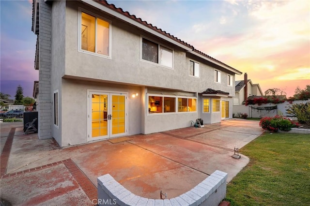 back of property at dusk featuring a patio, stucco siding, a tile roof, and french doors