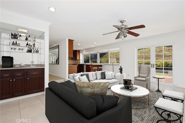 living room with wet bar, baseboards, a ceiling fan, light tile patterned floors, and crown molding