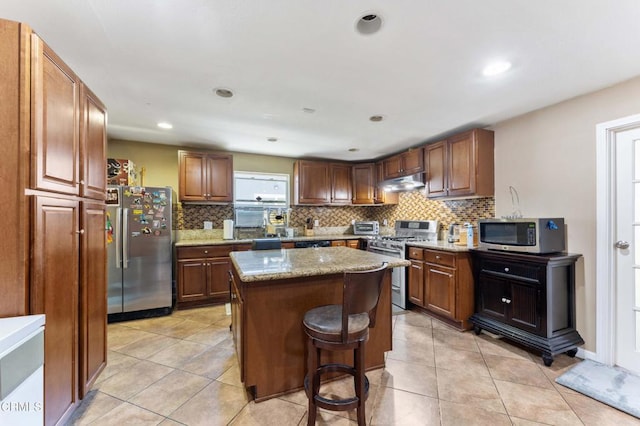 1421 E Abbottson St, Carson, CA 90746 - kitchen with appliances with stainless steel finishes, under cabinet range hood, decorative backsplash, a center island, and light stone countertops