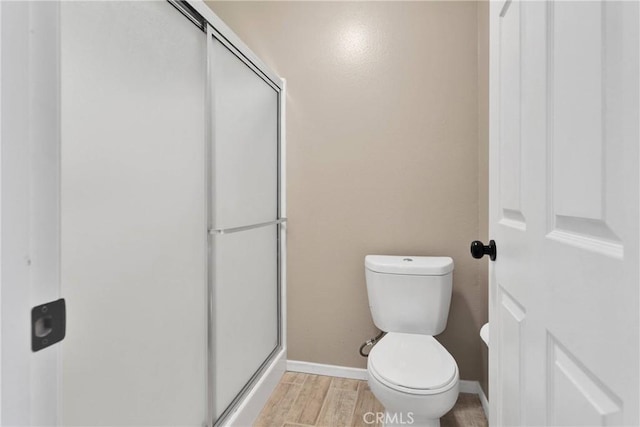 bathroom featuring baseboards, toilet, wood finished floors, and a stall shower