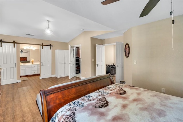 bedroom featuring a barn door, lofted ceiling, visible vents, and light wood-type flooring
