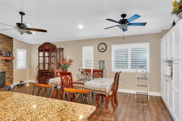 dining room with a ceiling fan, baseboards, a fireplace, and dark wood-type flooring