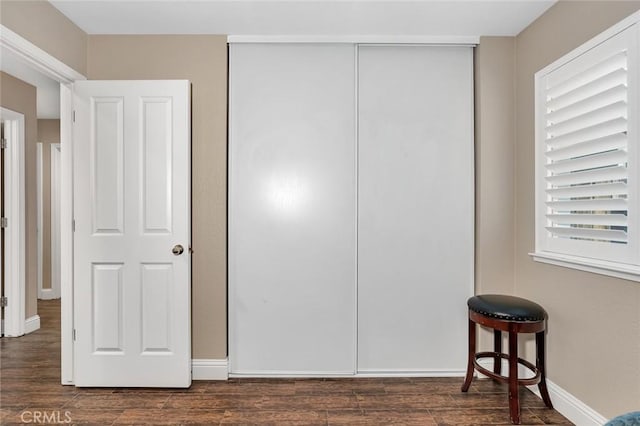 unfurnished bedroom featuring baseboards, dark wood-type flooring, and a closet