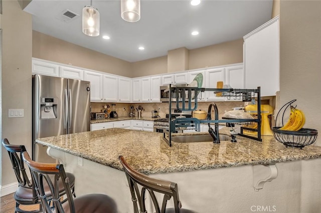 kitchen with a sink, stainless steel appliances, a peninsula, white cabinetry, and light stone countertops