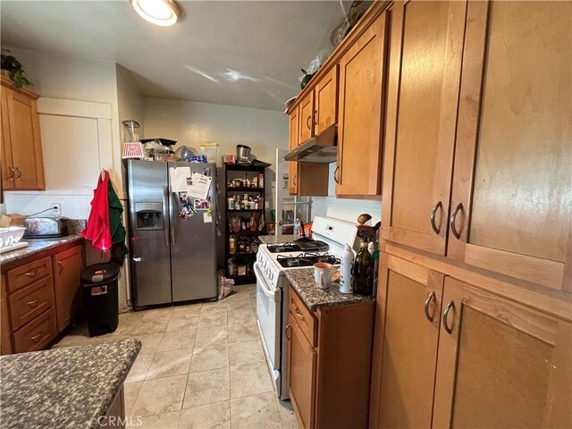 3852 4th St, Riverside, CA 92501 - kitchen with white gas stove, dark stone countertops, brown cabinetry, stainless steel fridge, and under cabinet range hood