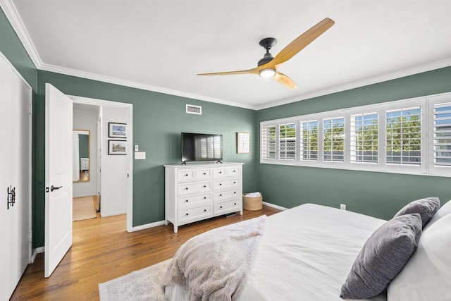 bedroom with wood finished floors, visible vents, crown molding, and baseboards
