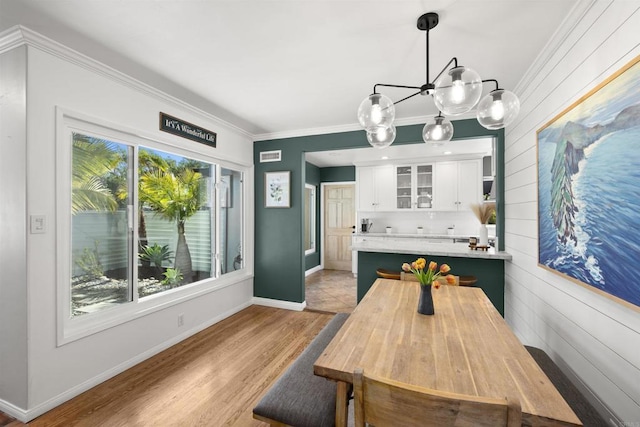 dining room featuring wooden walls, ornamental molding, baseboards, a chandelier, and light wood-style flooring