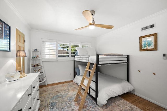 bedroom with baseboards, visible vents, a ceiling fan, wood finished floors, and ornamental molding