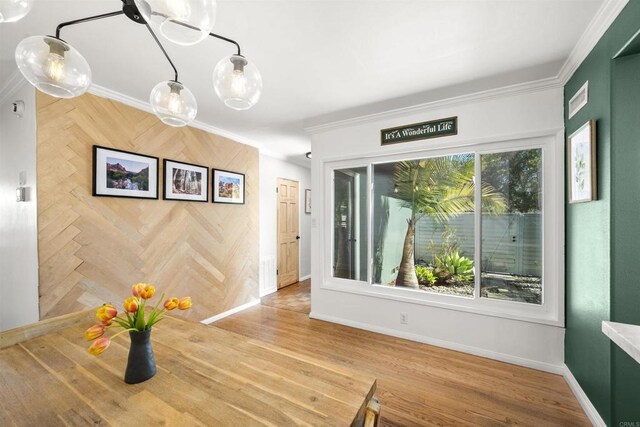 unfurnished dining area featuring wood finished floors, visible vents, crown molding, and baseboards