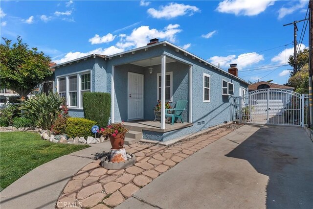 view of front of property featuring stucco siding, a gate, a chimney, covered porch, and driveway