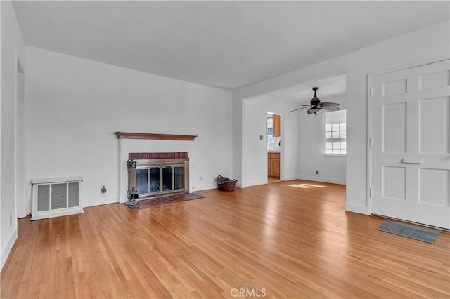 unfurnished living room featuring a brick fireplace, ceiling fan, visible vents, and light wood finished floors