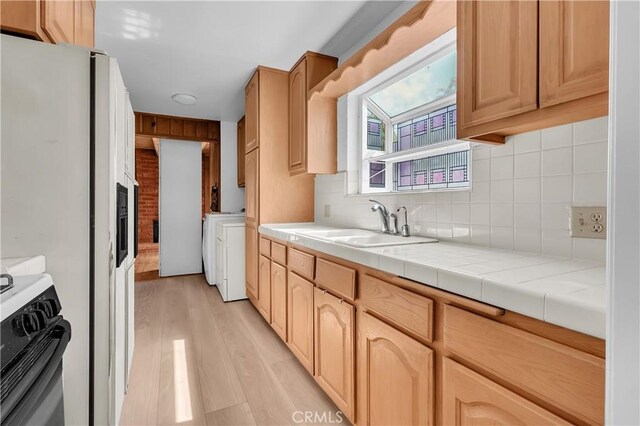 kitchen with a sink, light wood-style floors, stove, tile countertops, and tasteful backsplash