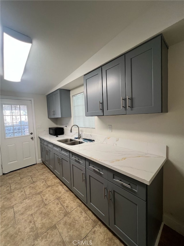 kitchen featuring a wealth of natural light, gray cabinetry, light stone countertops, and a sink