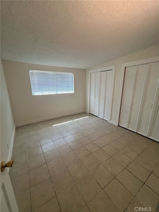 unfurnished bedroom featuring tile patterned flooring, multiple closets, a textured ceiling, and baseboards