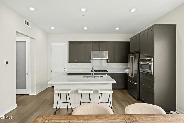 26945 Nature View Pl, Valencia, CA 91381 - kitchen with appliances with stainless steel finishes, a sink, dark wood finished floors, light countertops, and an island with sink