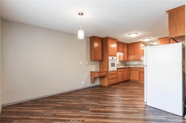 kitchen with brown cabinetry, dark wood-style flooring, pendant lighting, under cabinet range hood, and white appliances