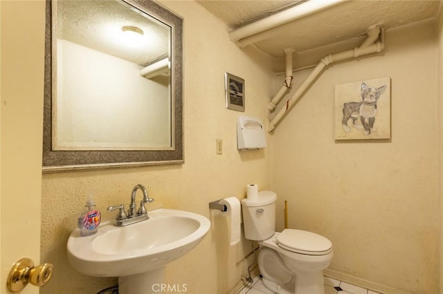 bathroom with a textured ceiling, a sink, baseboards, tile patterned floors, and toilet