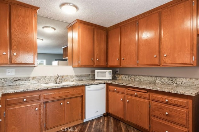 kitchen featuring brown cabinetry, dark wood-style flooring, white appliances, a textured ceiling, and a sink