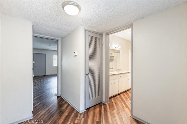 hall with baseboards, a textured ceiling, and wood finished floors