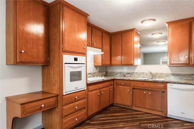 kitchen with white appliances, brown cabinets, a sink, and dark wood-type flooring