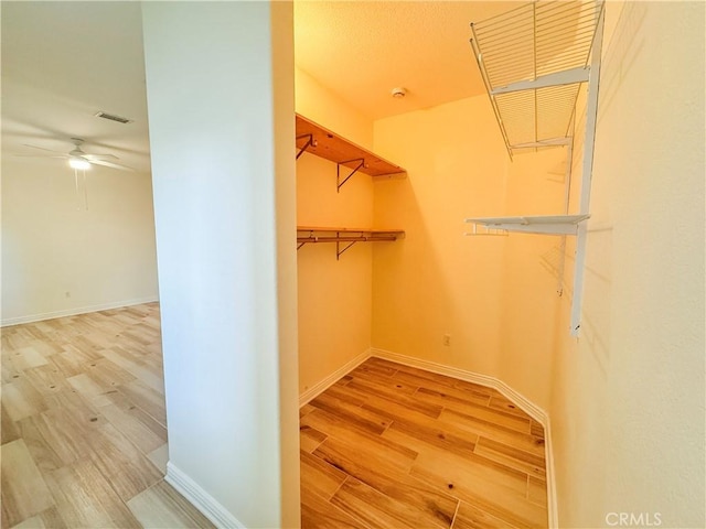 walk in closet featuring wood finished floors, visible vents, and a ceiling fan