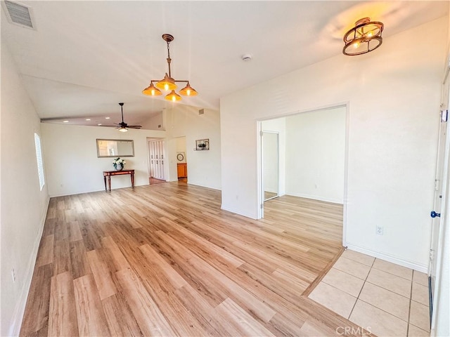 unfurnished living room with vaulted ceiling, ceiling fan with notable chandelier, light wood-style floors, baseboards, and visible vents