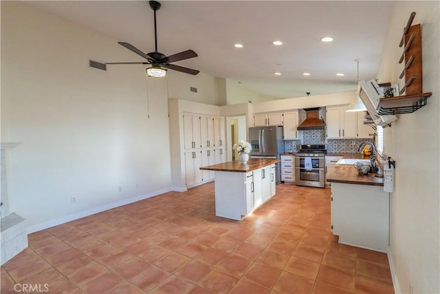 kitchen featuring vaulted ceiling, visible vents, wall chimney exhaust hood, wood counters, and appliances with stainless steel finishes