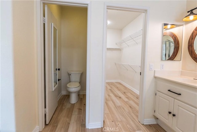 bathroom with a walk in closet, wood finished floors, toilet, and vanity