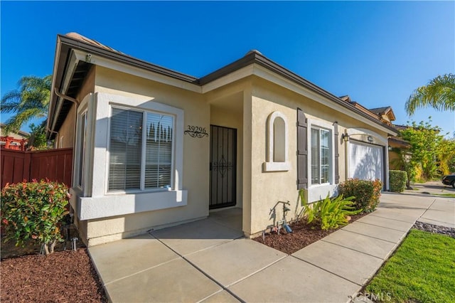 view of front of house with fence, a garage, and stucco siding