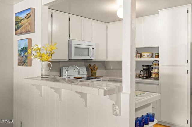 kitchen with tile counters, white cabinets, white appliances, a peninsula, and a breakfast bar area