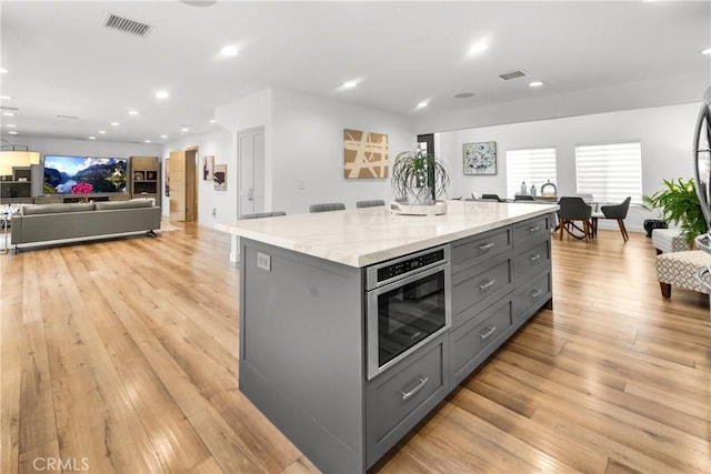 26011 Redbluff Dr, Calabasas, CA 91302 - kitchen with light stone counters, light wood finished floors, visible vents, a kitchen island, and gray cabinets