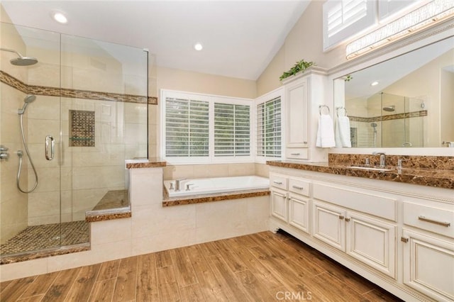 full bath with vaulted ceiling, wood finished floors, a shower stall, a garden tub, and vanity