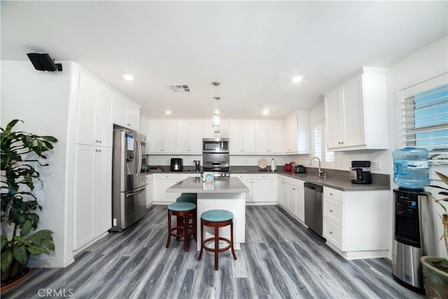 kitchen with a sink, a center island with sink, visible vents, wood finished floors, and appliances with stainless steel finishes