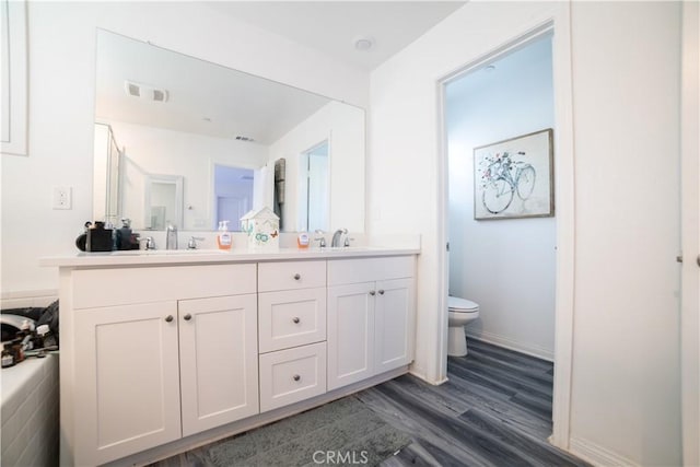 bathroom with double vanity, toilet, wood finished floors, and a sink