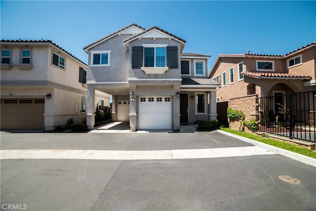 view of front of home with fence, a tiled roof, stucco siding, an attached garage, and driveway