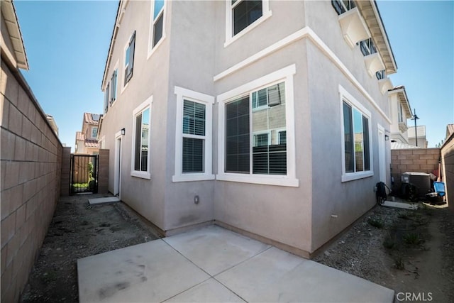 view of home's exterior featuring a gate, central AC, fence private yard, a patio, and stucco siding