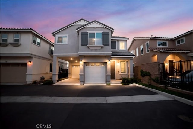 traditional home featuring a garage, fence, aphalt driveway, and stucco siding