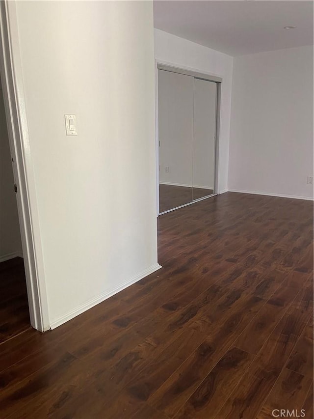 unfurnished room featuring baseboards and dark wood-style flooring