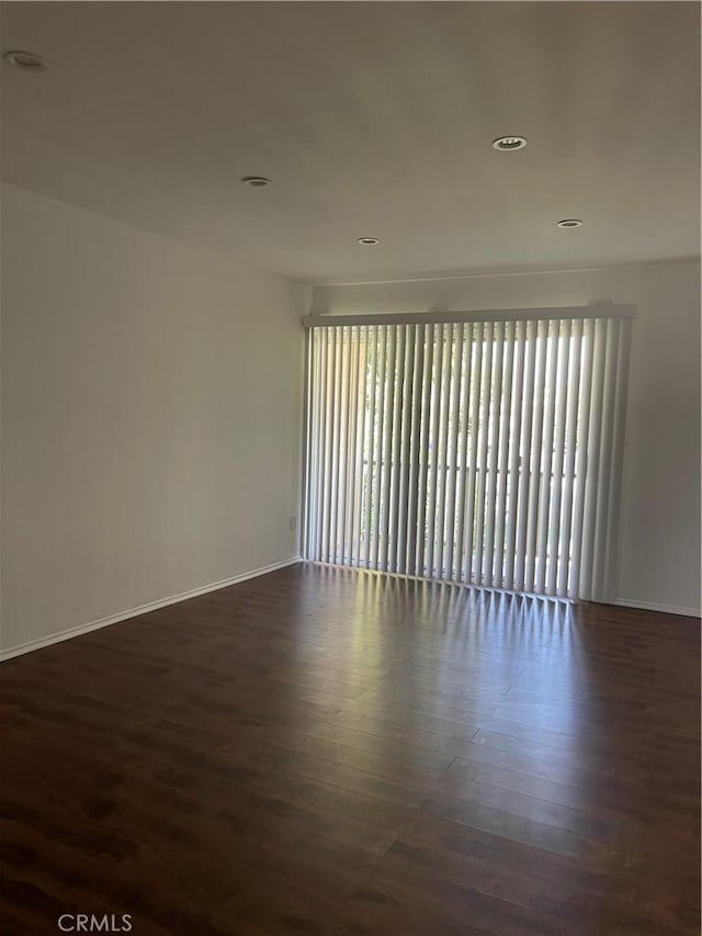 spare room with baseboards, recessed lighting, wood finished floors, and a wealth of natural light