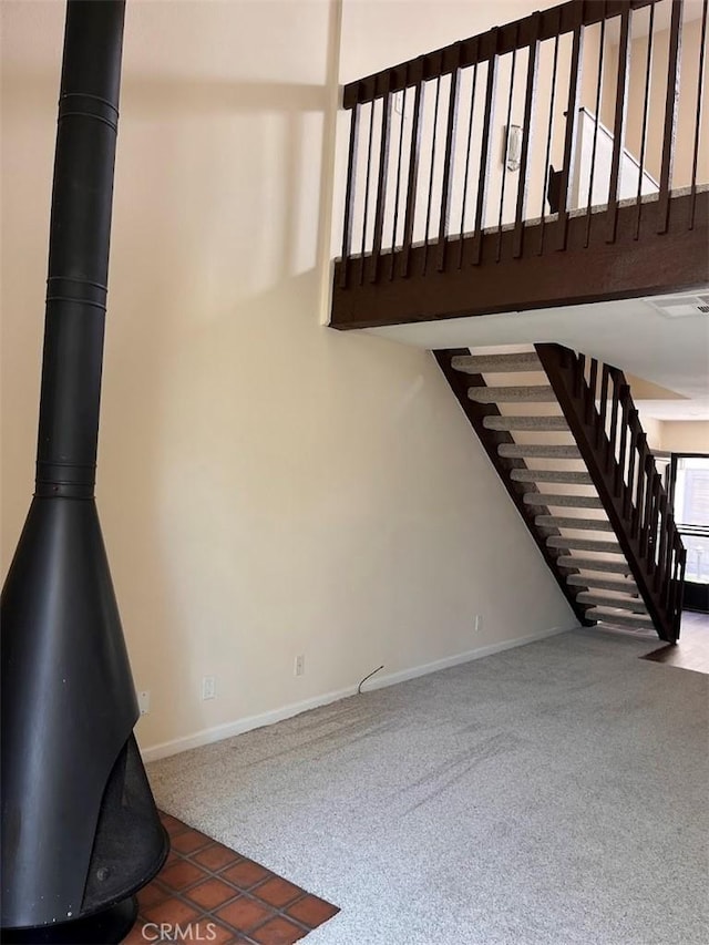 12750 Centralia St Unit 142, Lakewood, CA 90715 - unfurnished living room featuring carpet flooring, baseboards, a towering ceiling, stairway, and a wood stove